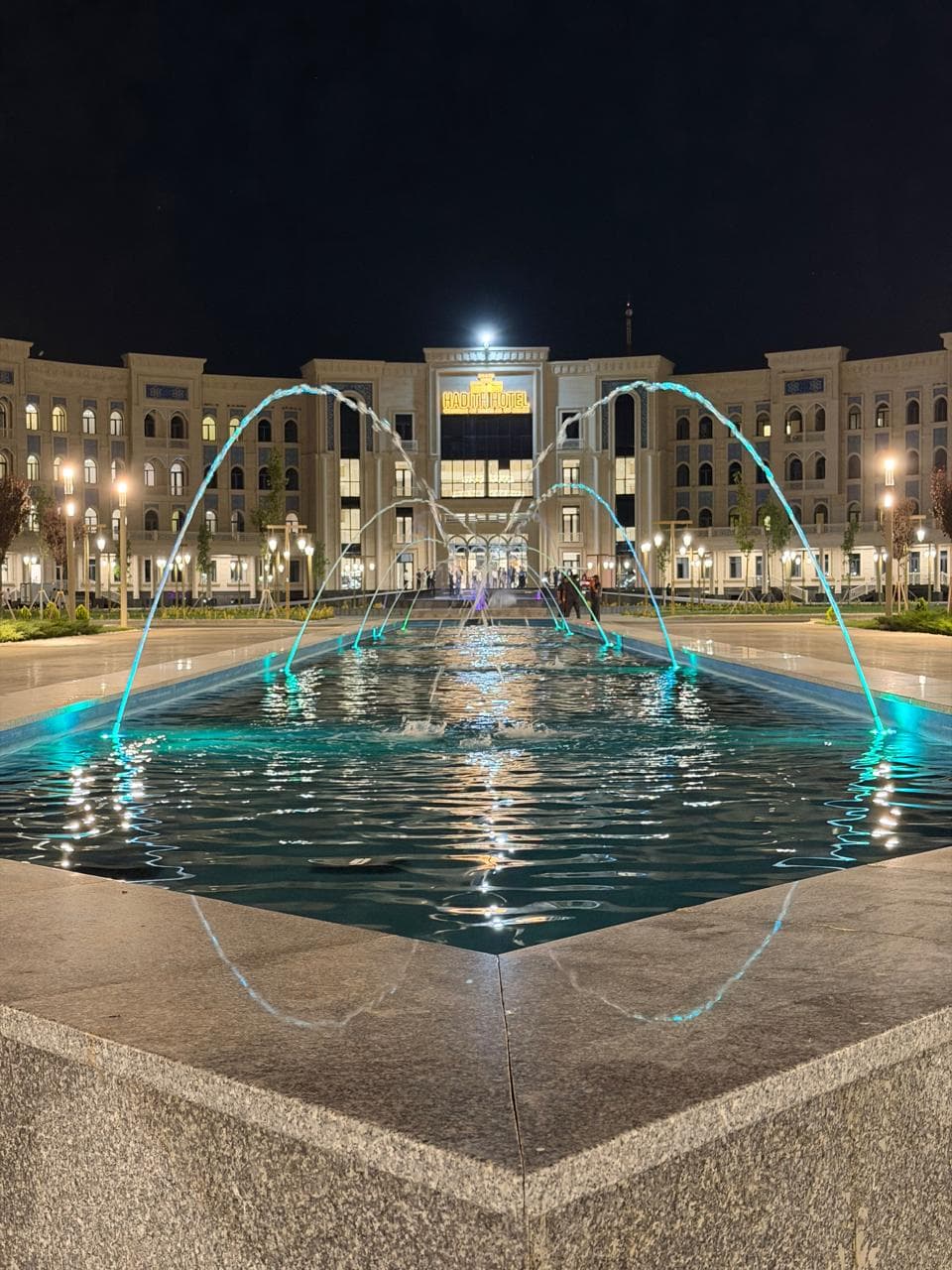 Hadith Hotel illuminated at night behind its fountains