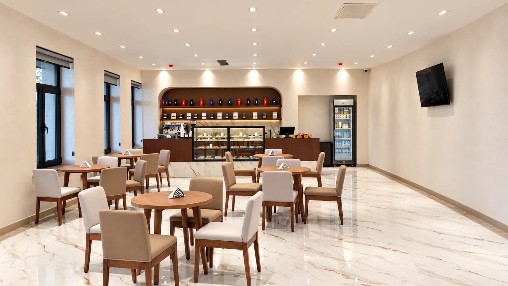 Coffee lounge with cream chairs, round tables, and a pastry counter.